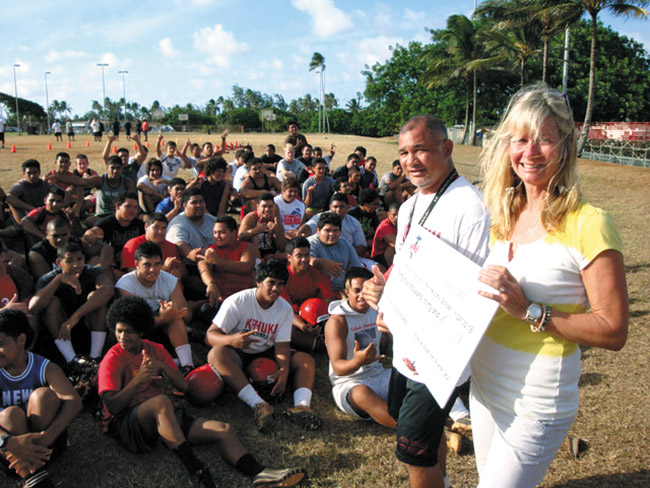 Kahuku.org manager Alicia Esche displays the symbolic $34,000 from store profits to coach Reggie Torres and football team. Photo from KC Connors.