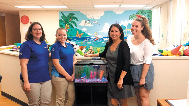 PetSmart employees Tabitha Pratt (from left) and Jessica Vogelhut with Mary Saunders, Family Promise of Hawaii executive director, and volunteer coordinator Lauren Balkin - and the new aquarium. Photo courtesy of PetSmart. 