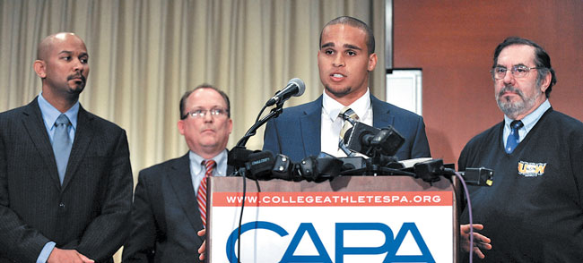 Kain Colter (at podium) speaks about unionizing players at a Jan. 28 news conference in Chicago, while College Athletes Players Association president Ramogi Huma (left), United Steel Workers national political director Tim Waters (second from left), and United Steel Workers president Leo Gerard look on  |  AP Photo/Paul Beaty