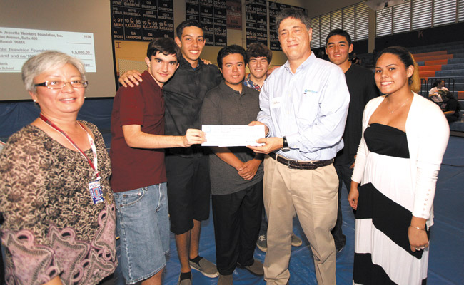 Kalaheo High teacher Kathy Shigemura (left) and her students present a $5,000 Educating the Heart grant to PBS Hawaii's 'Hiki No' producer Robert Pennybacker (center) during the school's senior farewell assembly. Students include (from left) Houston Lowry, Connor Doane, Joshua Ballesteros, Carson Chiu, Thomas Capllonch and Sierra Freitas. Not pictured: Shauna Perry. Photo from PBS Hawaii. 