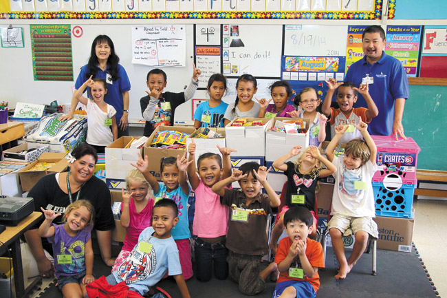 Laie Elementary School teacher Dionne Toelupe (seated, front) and her happy kindergarten class enjoy the gift of cool school supplies from Kuakini Heath System employees, represented by Donda Spiker (back, left) and Dayton Morinaga. Photo from Kuakini Health System. 
