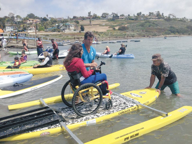Kailua native Kawika Watt hands a paddle to a woman on an Onit Ability Board at Oceanside Harbor in San Diego PHOTO COURTESY ONIT ABILITY BOARDS