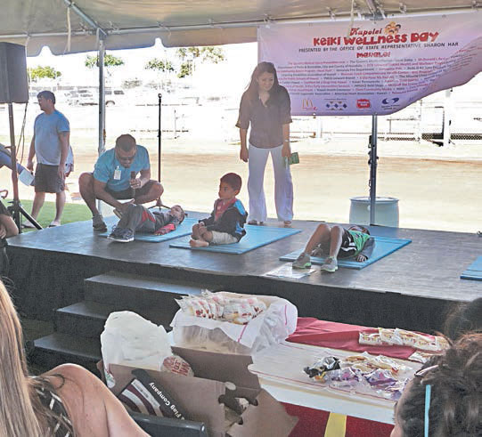 (above left, in blue) Rob Hesia from state Department of Education’s Leeward District Health and Wellness Program and Rep. Sharon Har (standing) watch over 5-year-old keiki competing in a sit-up competition at Kapolei Keiki Wellness Day. PHOTOS FROM REP. HAR’S OFFICE.