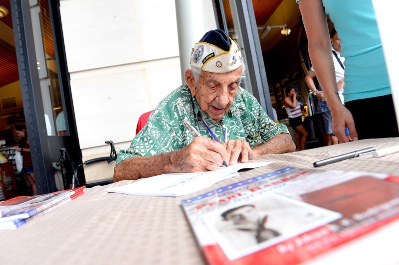 Pearl Harbor survivor Alfred B.K. Rodrigues signs a book for visitors at Pearl Harbor Visitor Center 